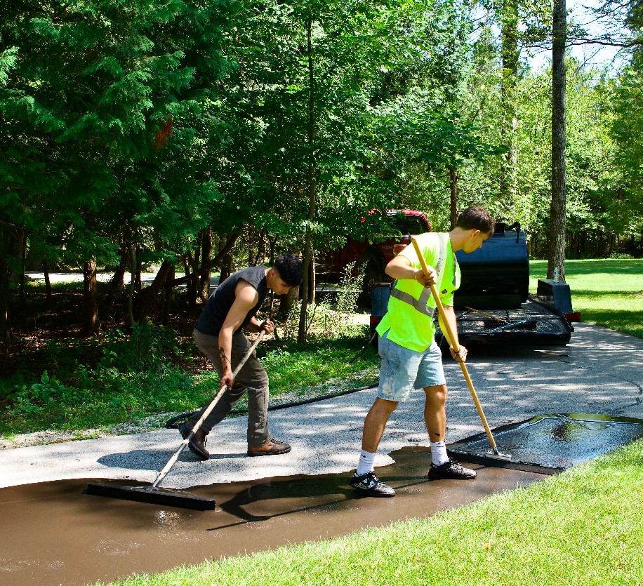 C&G Asphalt Sealcoating team members applying sealcoat to a residential driveway
